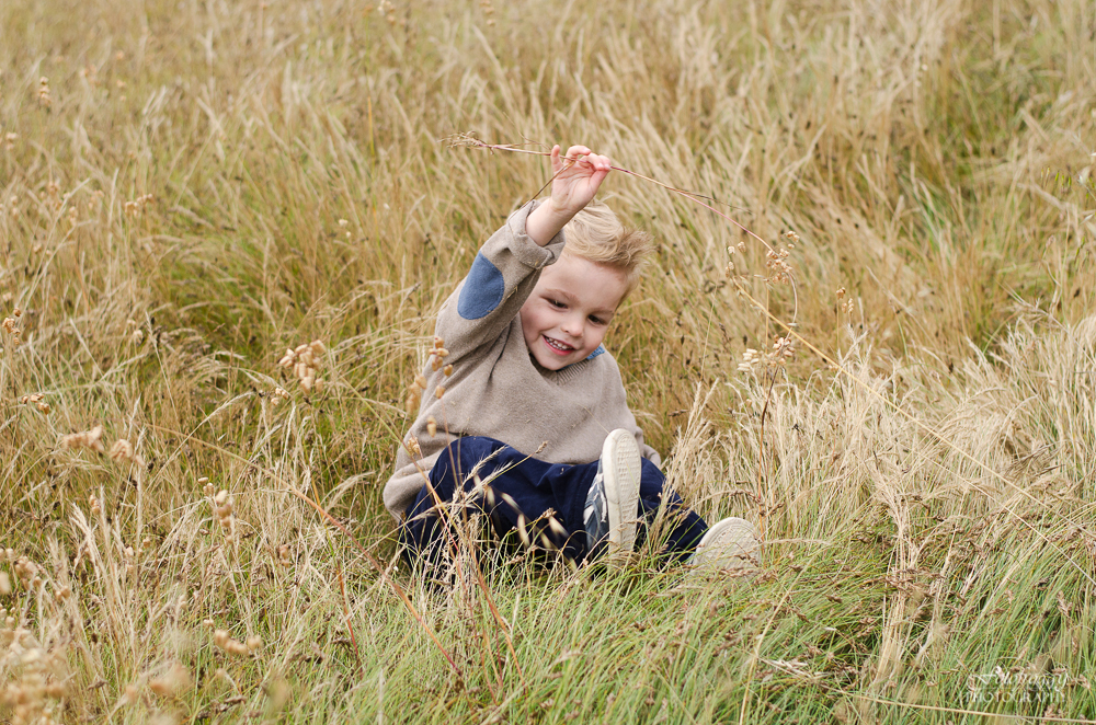 Cute little boy in beige and blue playing in tall grass Pacific Grove portraits