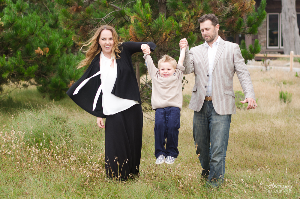 Dad and Mom swinging happy little boy in beige sweater Pacific Grove portraits