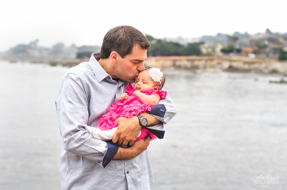Sweet portrait father kissing baby girl in pink ruffles oceanview Pacific Grove, Ca