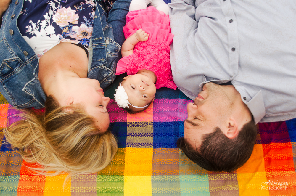 Baby girl in pink laying with parents on bright plaid blanket