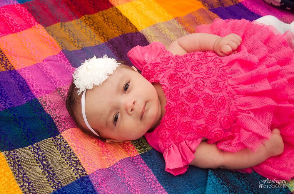 Sweet baby girl in pink ruffled dress lying on bright colorful blanket Monterey family photos