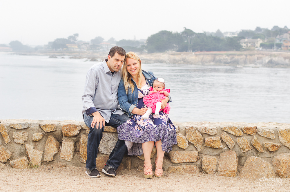 Cute family photo blue and pink sitting on rock wall by ocean Monterey Bay Ca